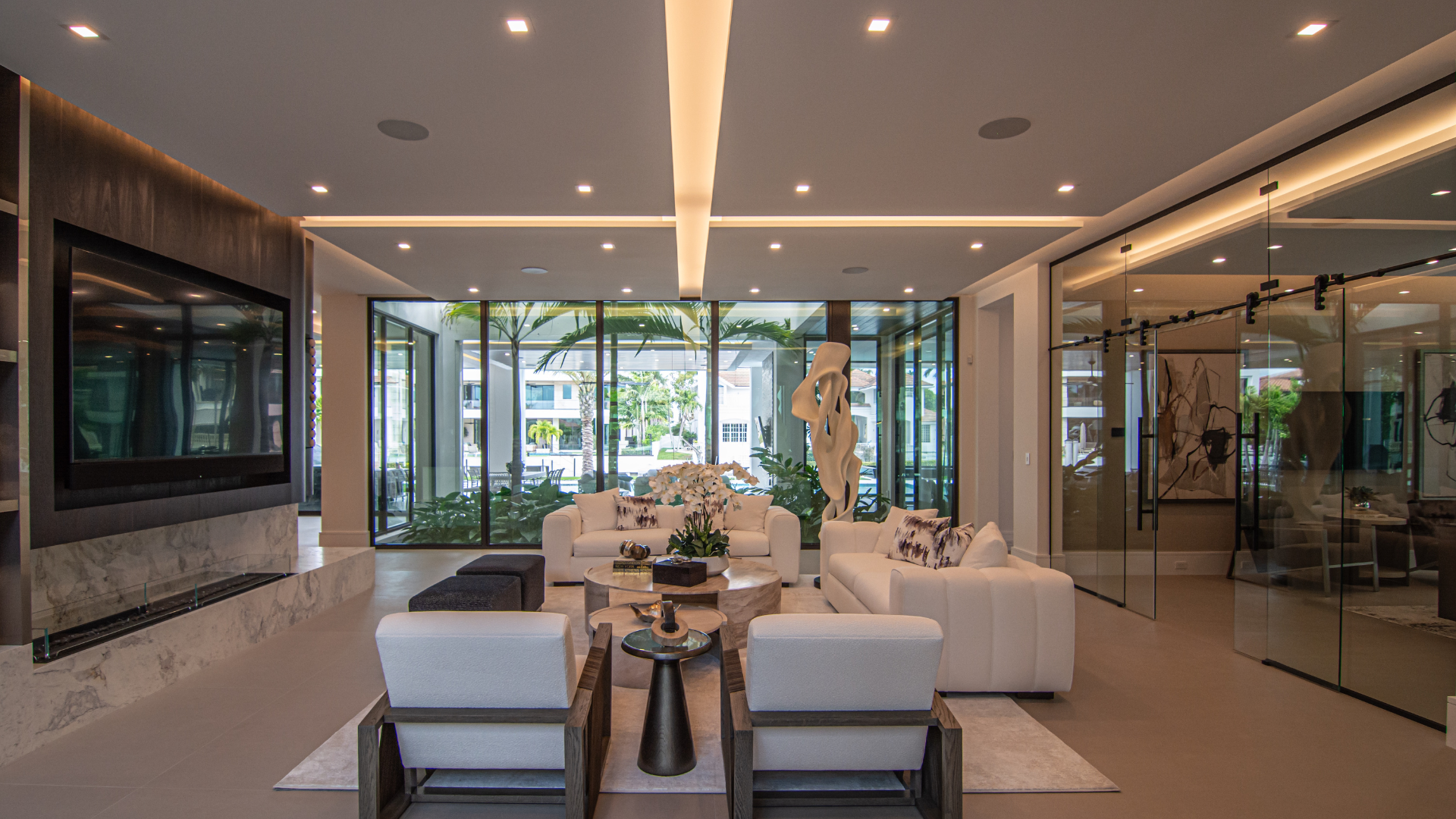 Open living room with sculpture, integrated television, and layered ceiling lighting