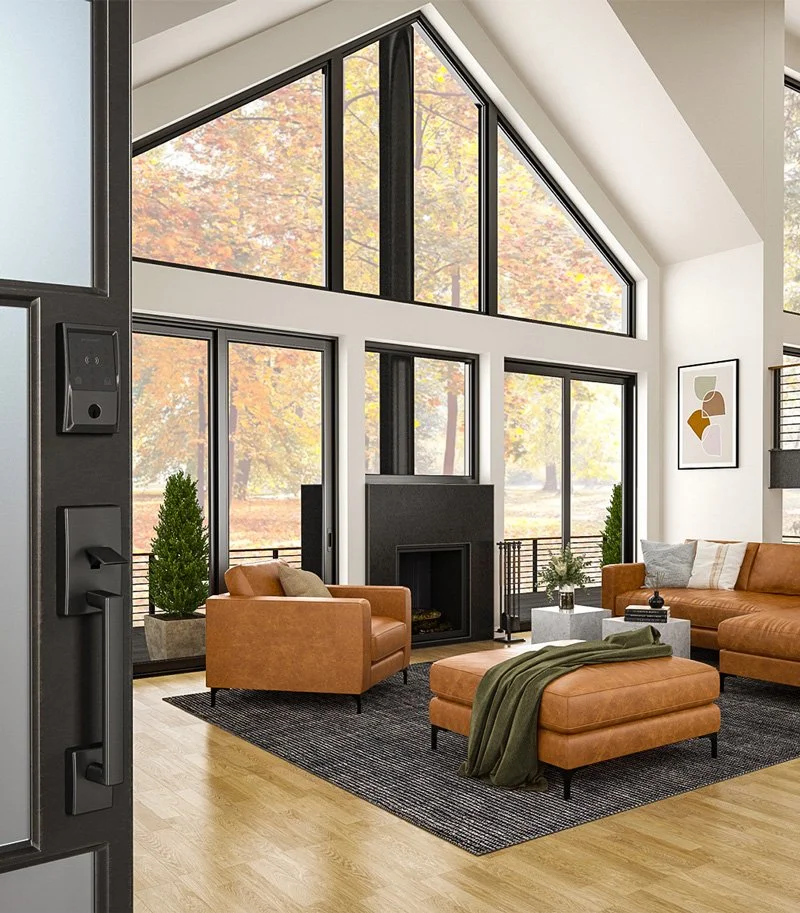 Modern living room with large floor-to-ceiling windows showing fall foliage outside, containing leather sofas, a black fireplace, a gray coffee table, and decor.