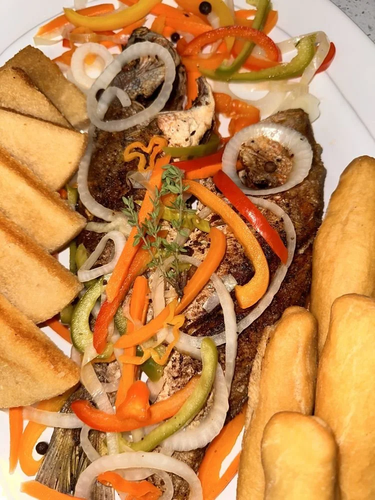 Fried fish with grilled vegetables, toast slices, and fried plantains on a white plate.