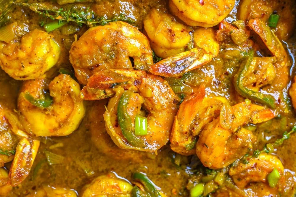 Close-up of spicy shrimp cooked with green bell peppers, onions, and herbs in a savory sauce.