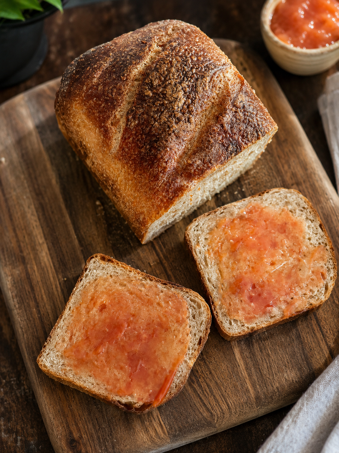 A loaf of bread with slices spread with melted butter on a wooden cutting board.