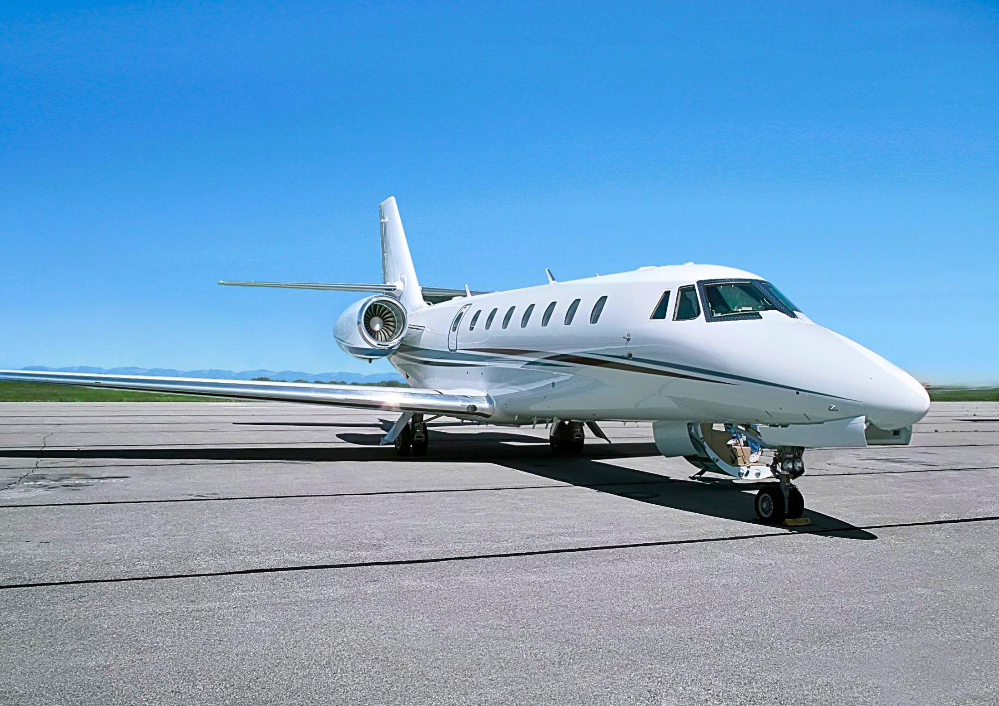 A white private jet airplane parked on an airport tarmac with a clear blue sky in the background.