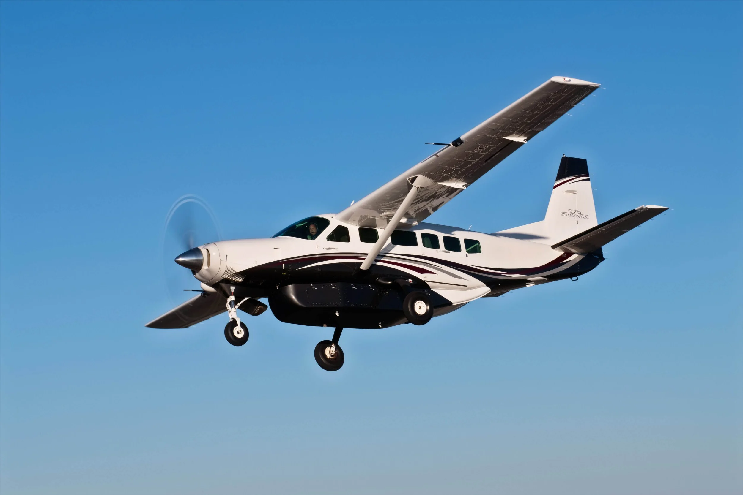Small single-engine airplane flying in clear blue sky, with landing gear visible, seen from below.