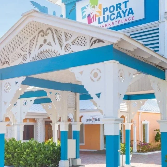 Entrance of Port Lucaya Marketplace with white and blue decorative wooden architecture and greenery.