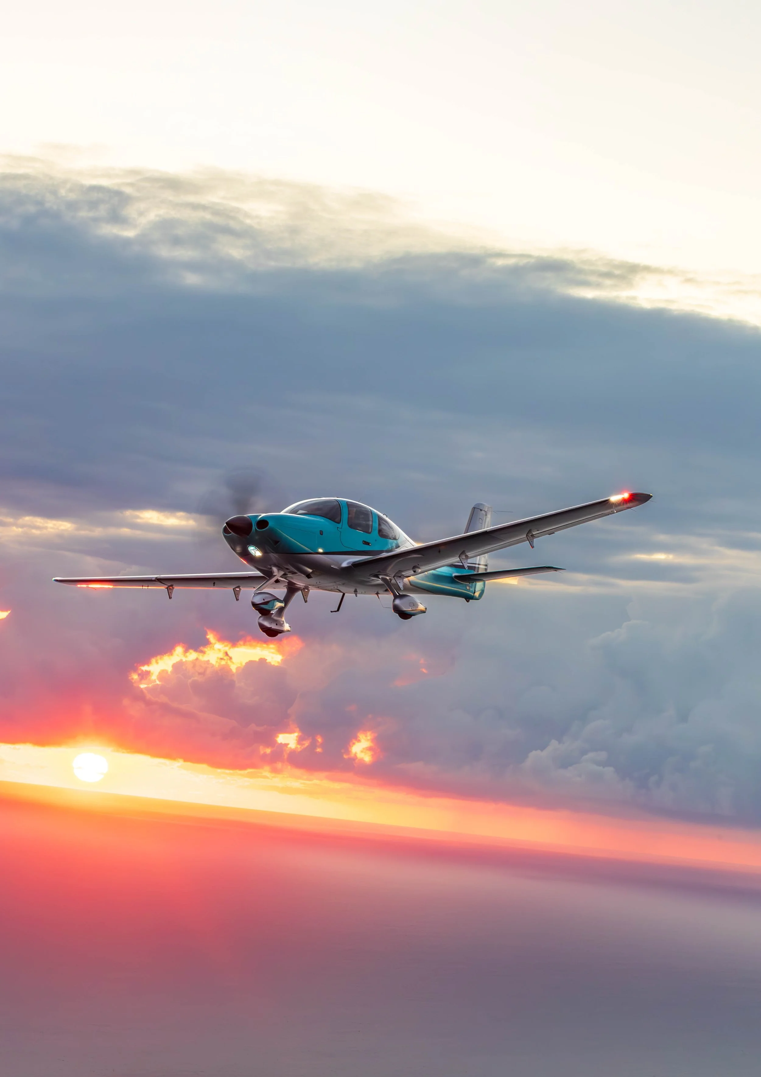 A small jet aircraft flying in a colorful sunset sky with clouds and the setting sun visible.
