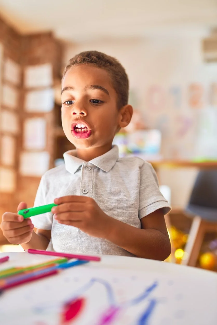 A young boy drawing with colorful markers at a table during speech therapy for late talkers in Bethesda, MD