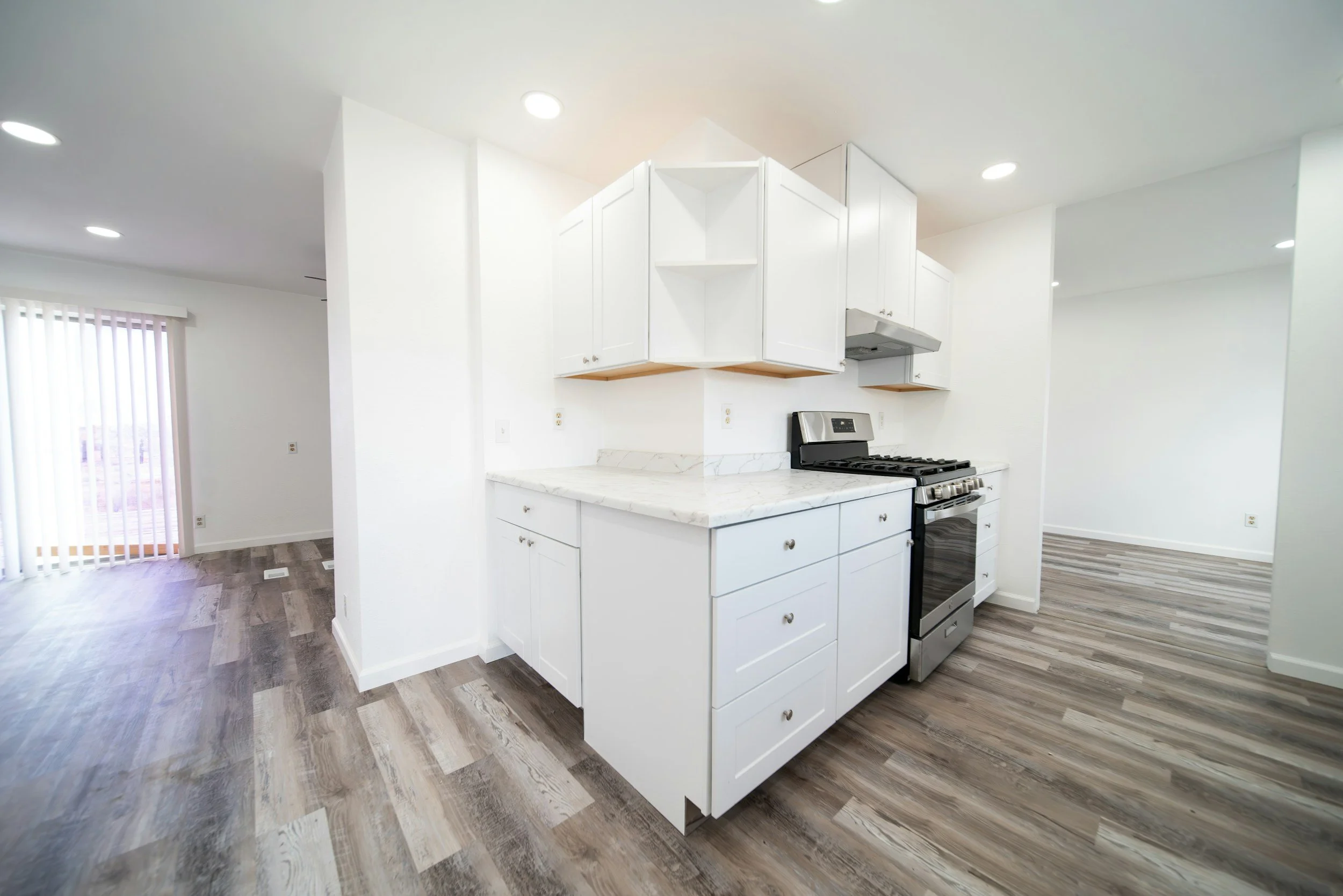 Kitchen area with white cabinets, a stainless steel stove, marble countertop, and wood laminate flooring in a bright room with a sliding glass door to the outside.