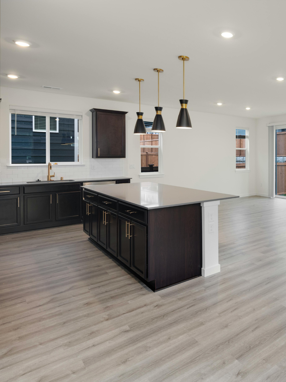 Modern kitchen with black cabinets, white countertops, pendant lights, a window above the sink, and light-colored wood flooring.
