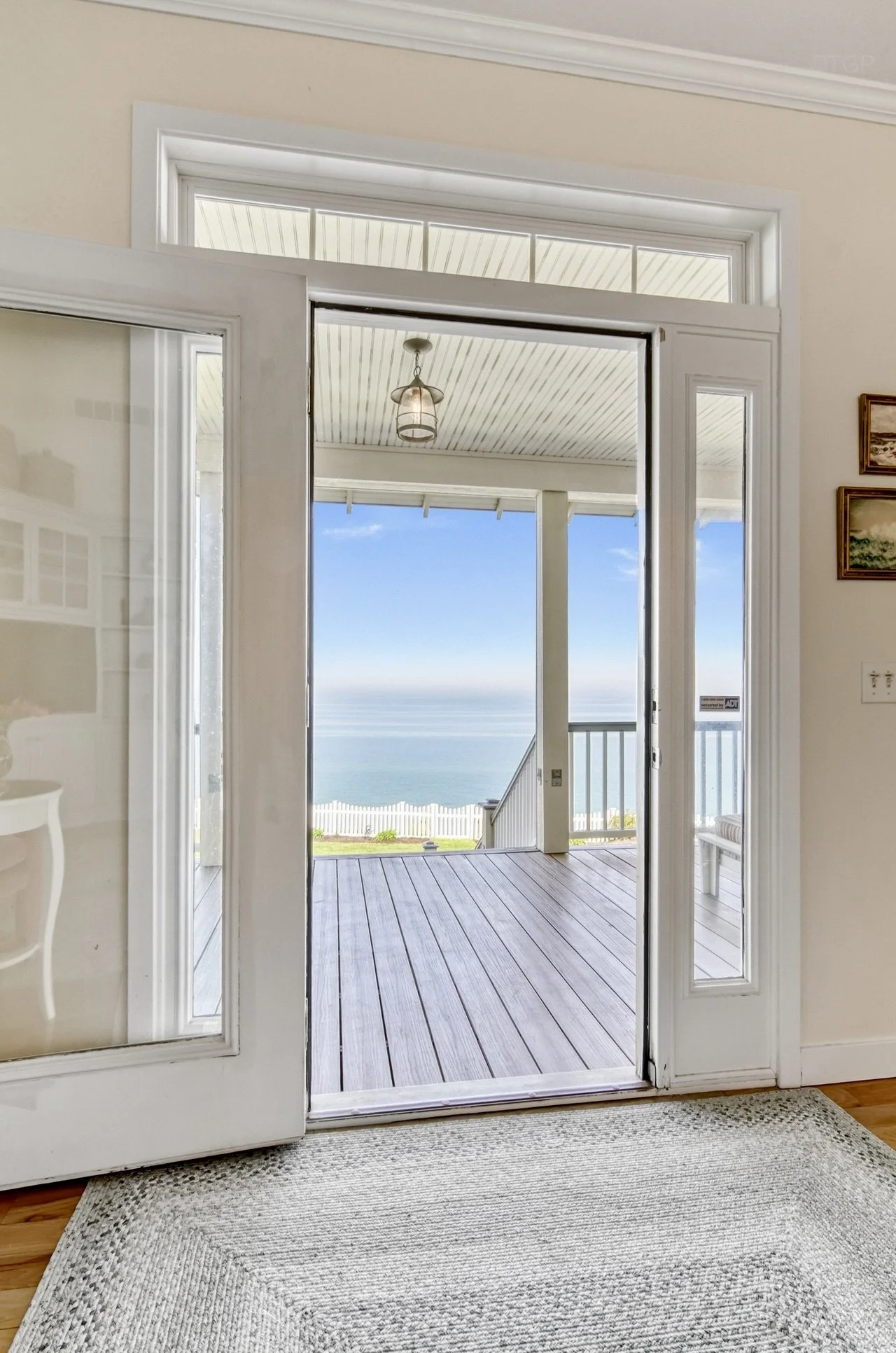 View from inside a house through a glass door opening to a porch with a wooden floor, railing, and a view of Lake Michigan and sky.