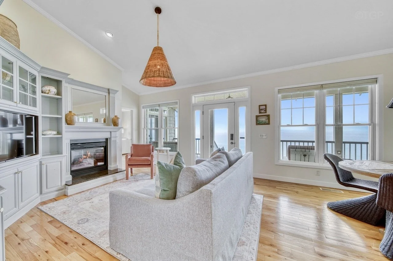 Living room with white walls, wooden floor, a beige sofa, a pink armchair, a fireplace, and large windows showing a view of a balcony and Lake Michigan.