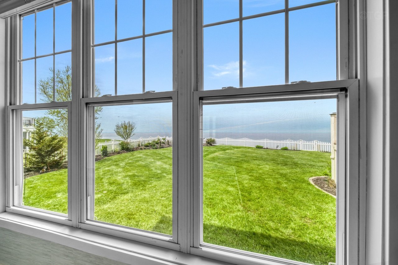 View of a green lawn with a white picket fence, trees, and shrubs seen through a large multi-pane window inside Haven House.