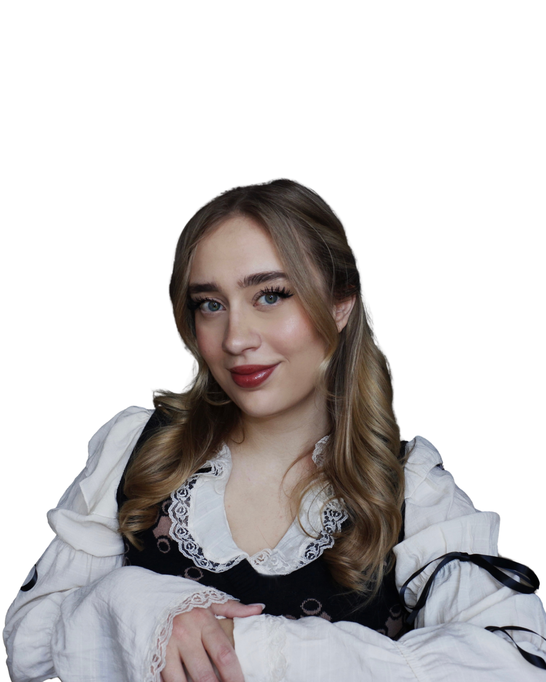 Portrait of a young woman with long, wavy blonde hair, blue eyes, and makeup including dark lipstick and eye makeup, wearing a white blouse and black dress with lace details, smiling against a black background.
