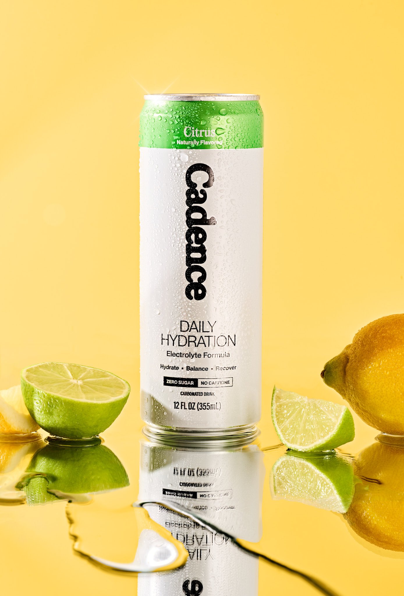 A can of C4 Daily Hydration electrolyte drink with lemon and lime slices and a lemon on a yellow background. Bright colorful CPG product photography for a modern food and beverage brand