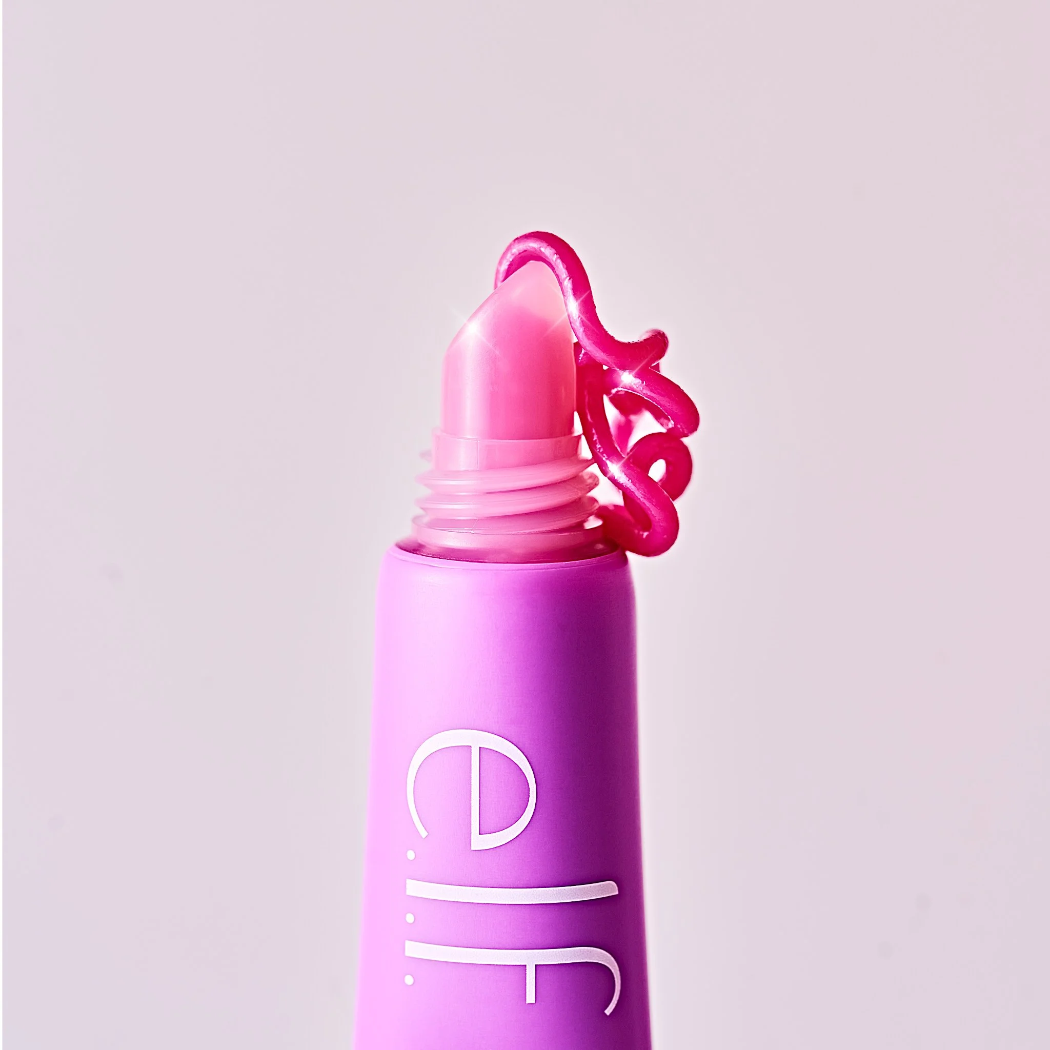 Close-up of a pink lipstick tube with the lid off, and a curled pink lipstick feathering out from the top. Brand name in white letters is visible vertically on the side of the tube for creative product CPG photography for elf cosmetics beauty 