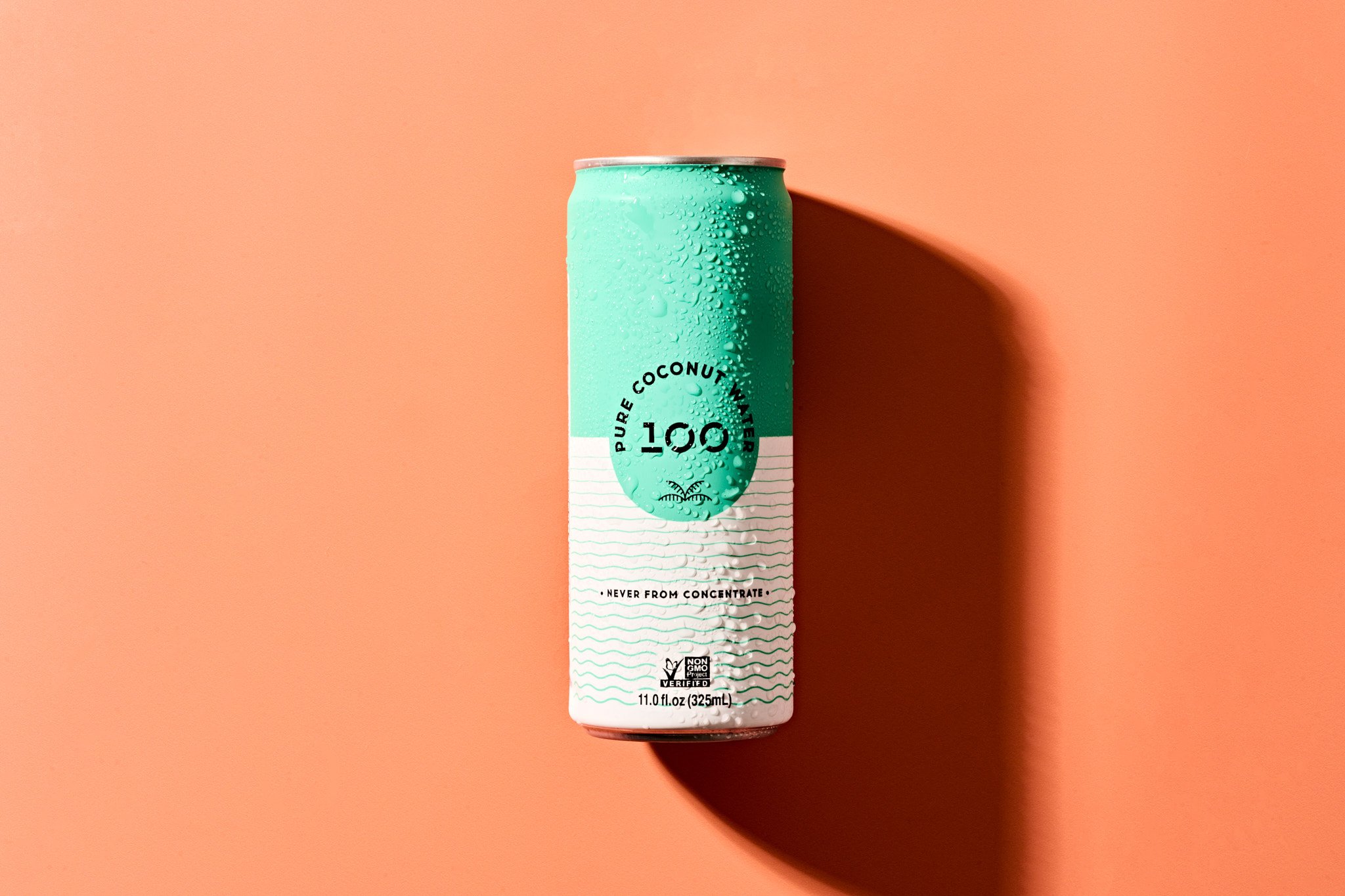 A can of Pure Coconut Water with condensation droplets on the surface, set against a pastel pink background, casting a shadow to the right. Commercial food and beverage photography for a modern consumer brand