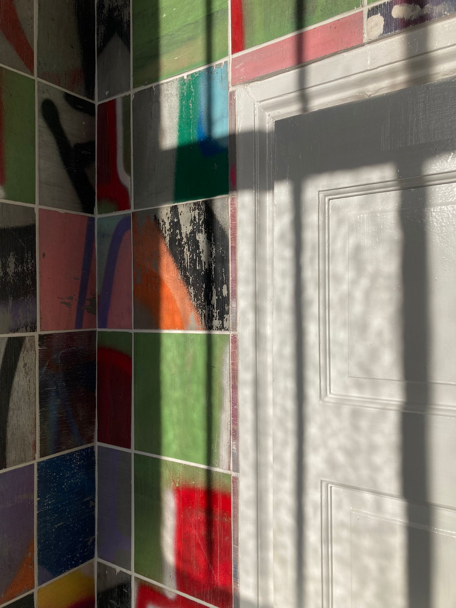 Colorful ceramic tiles on a wall with shadows cast on them.