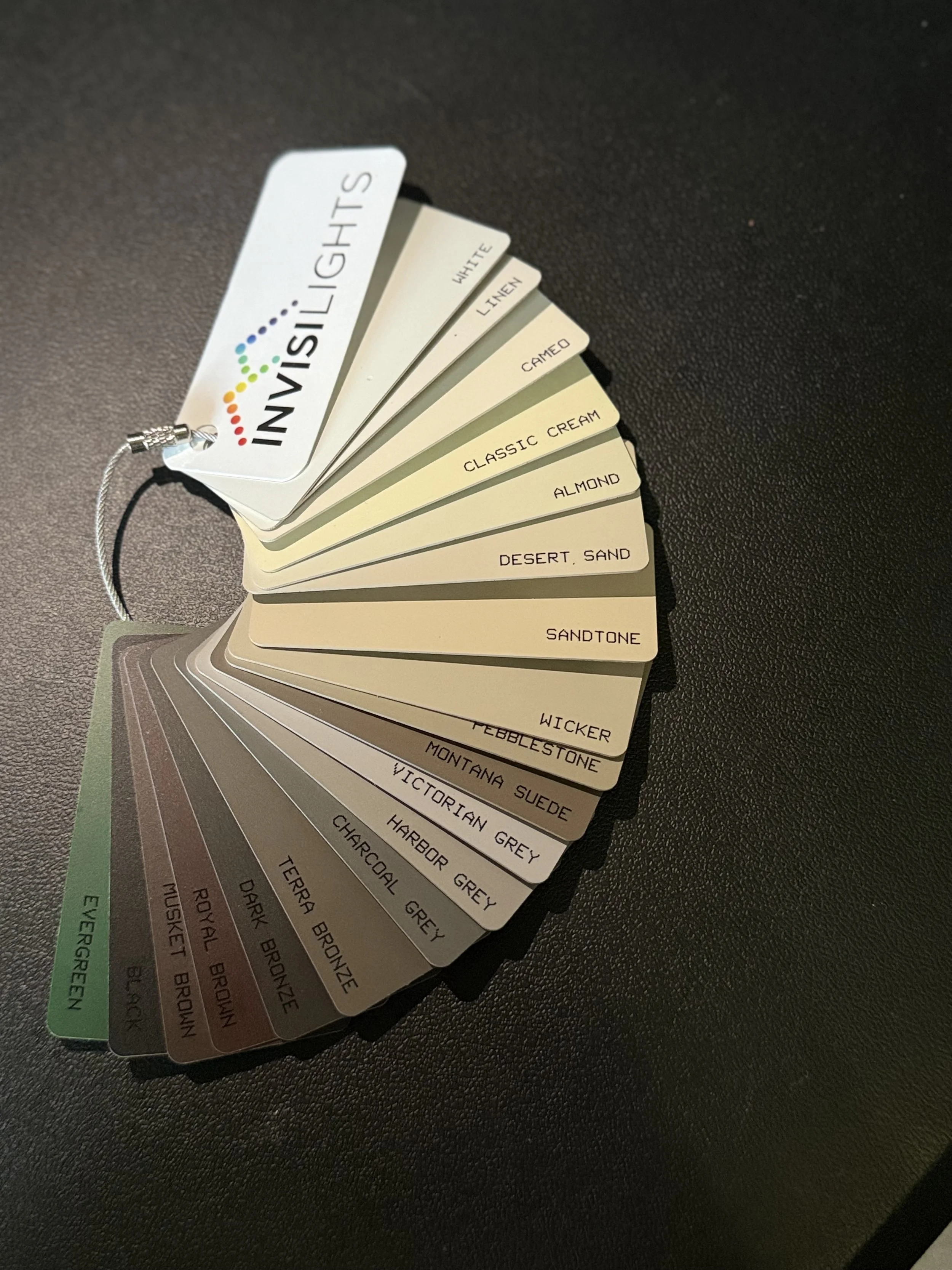 A fan deck of paint sample cards fanned out on a black surface, with each card displaying different shades and names of paint colors, including Classic Cream, Almond, Desert Sand, Sandtone, Wicker, and Victorian Grey.