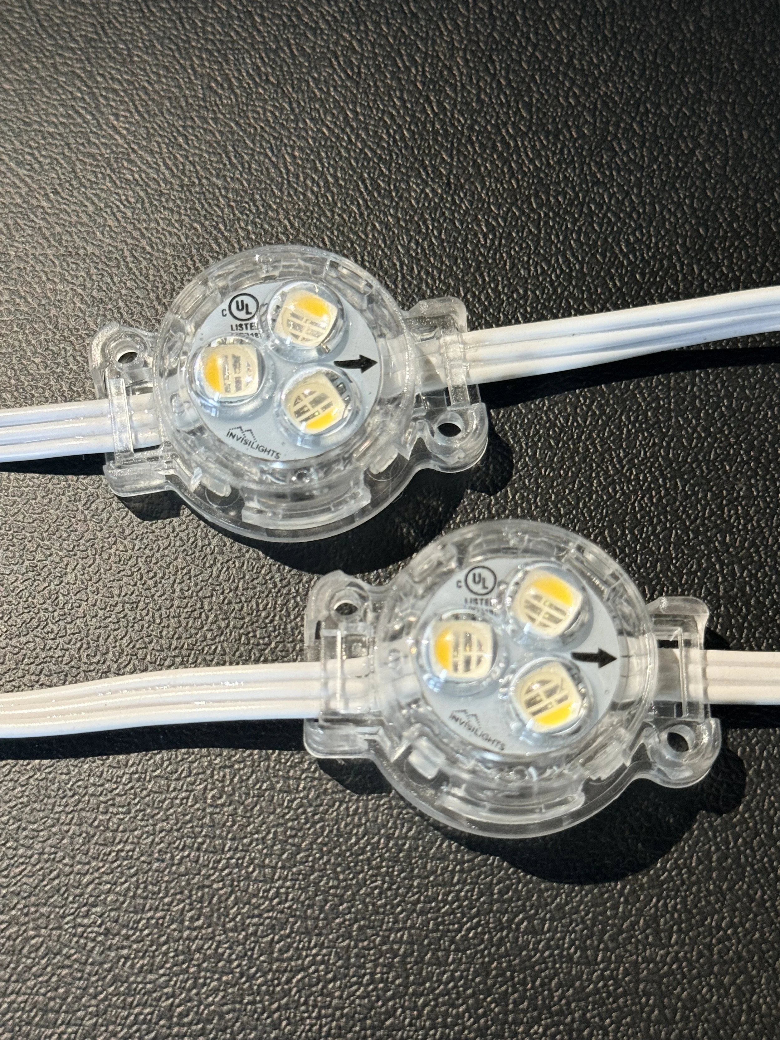 Close-up of LED lights in a transparent circular plastic fixture with white wiring on a black textured surface.