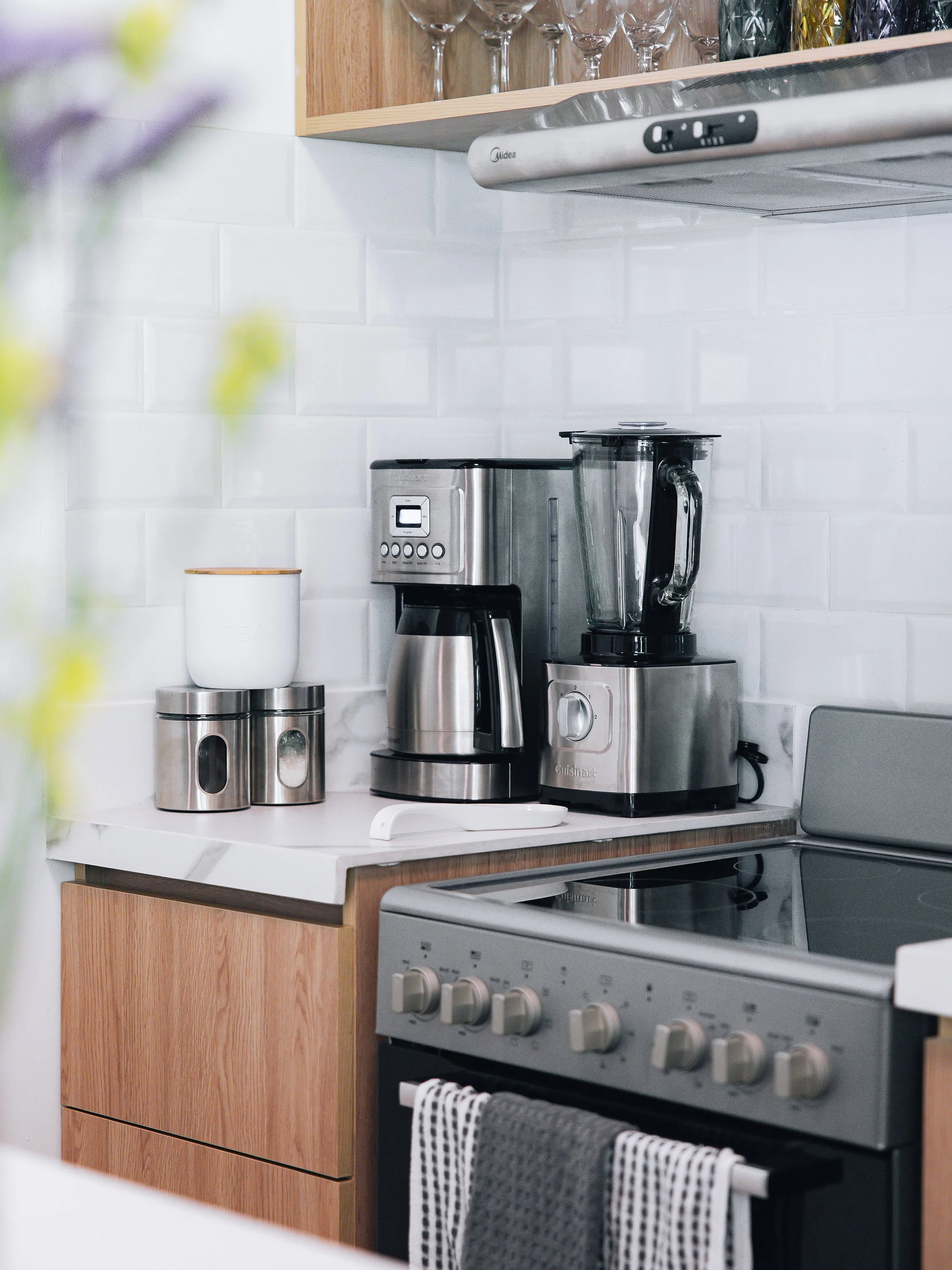 Kitchen counter with a blender, a toaster, and two canisters, with a wooden cabinet and a stove with control knobs in the background.