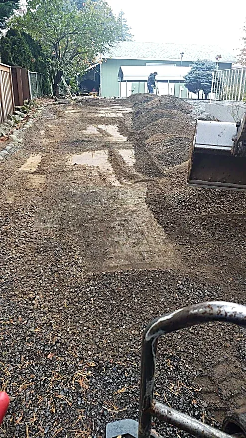 Backyard being leveled or prepared for landscaping or paving, with dirt piles, construction equipment, and a person working in the background.
