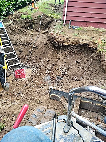 View of an active construction site with a large excavated area, construction equipment, and tools, next to a red building.