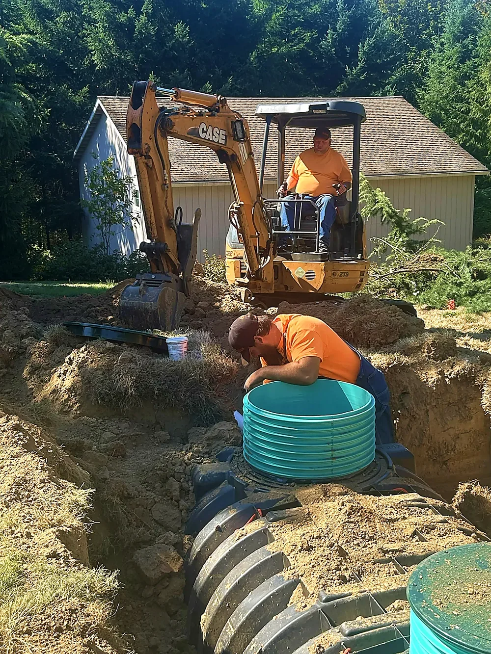 Workers installing underground piping with the help of excavator in a backyard.