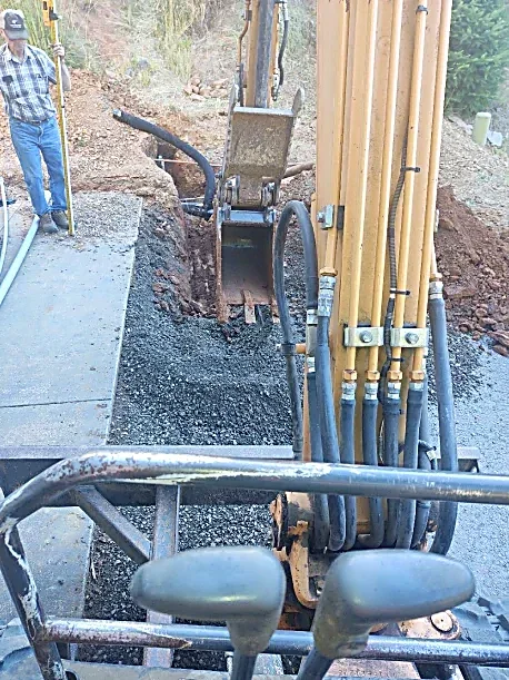 Construction site with an excavator digging a trench and a worker standing nearby.