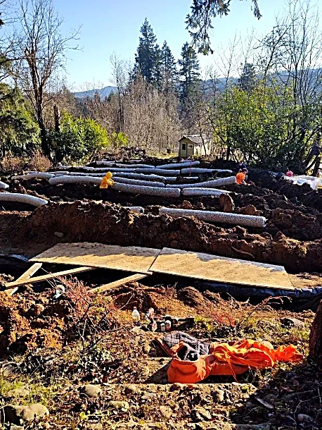 Construction site with pipes and equipment in a wooded area during daytime.