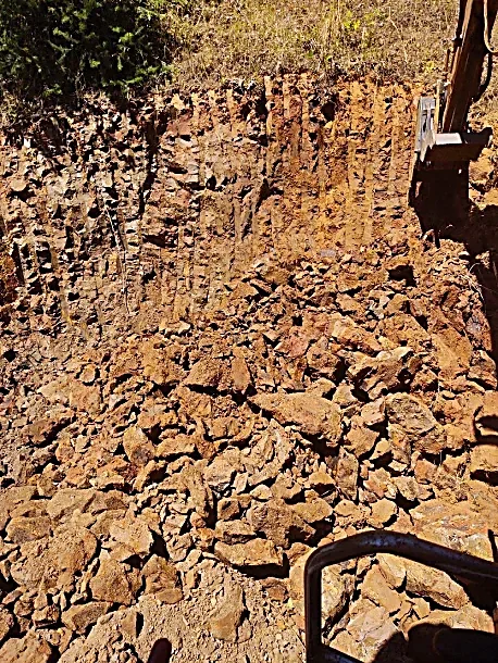 A construction site with a large area of disturbed earth and rocks, with brush and trees at the top edge of the image.