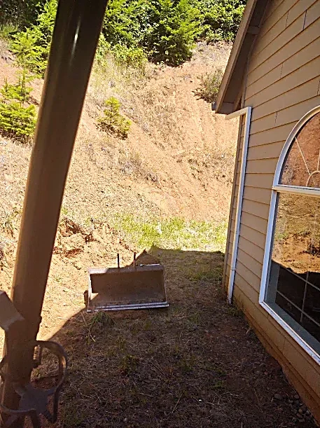 Backyard with a house, a window, and a snow shovel on the grass.