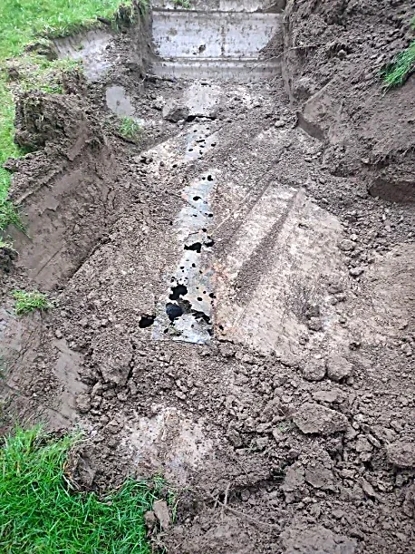 A hole in the ground along with a rusted metal piece covered in dirt and small debris, surrounded by excavated soil and grass.