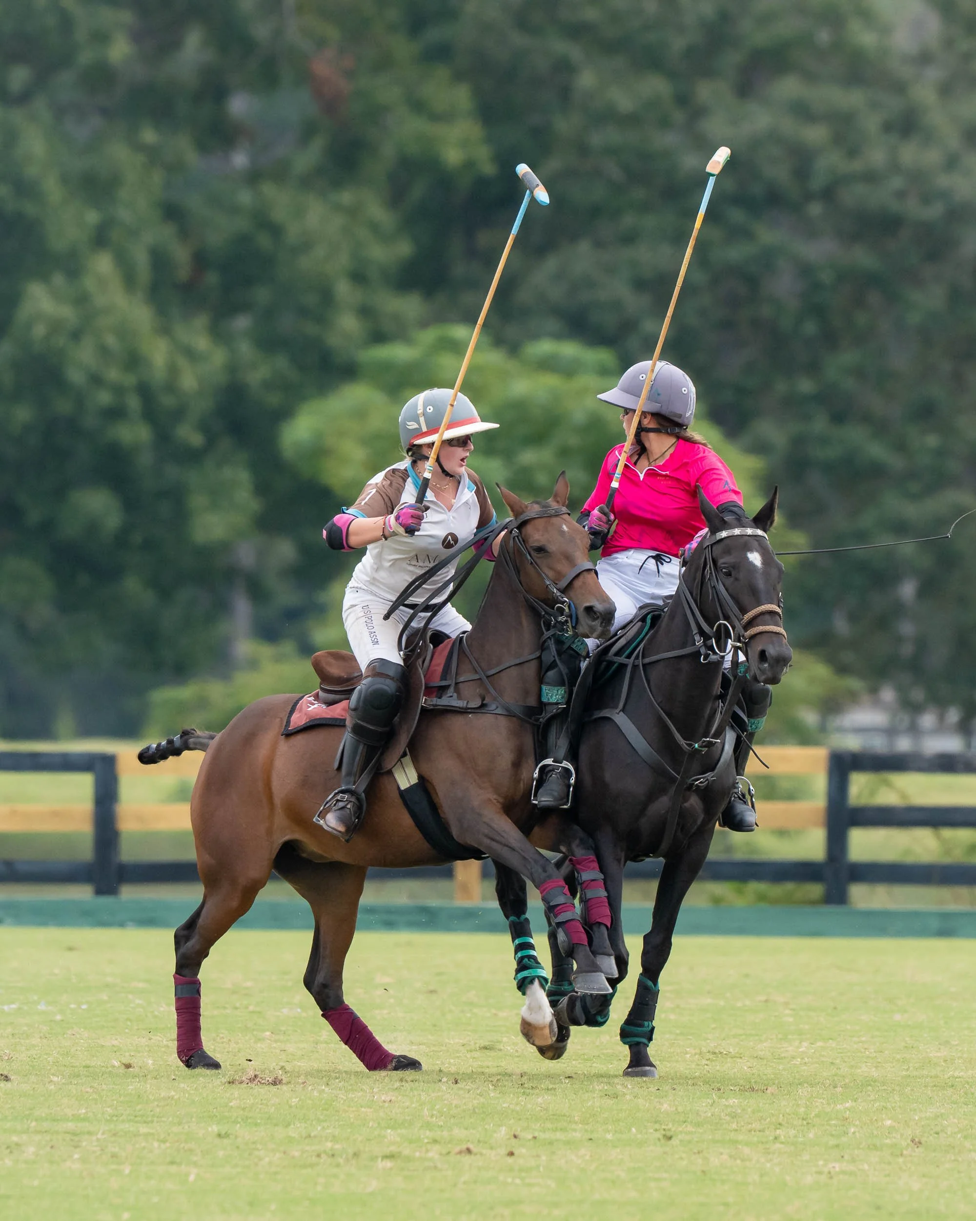 Two polo players riding horses and holding mallets on a grassy polo field