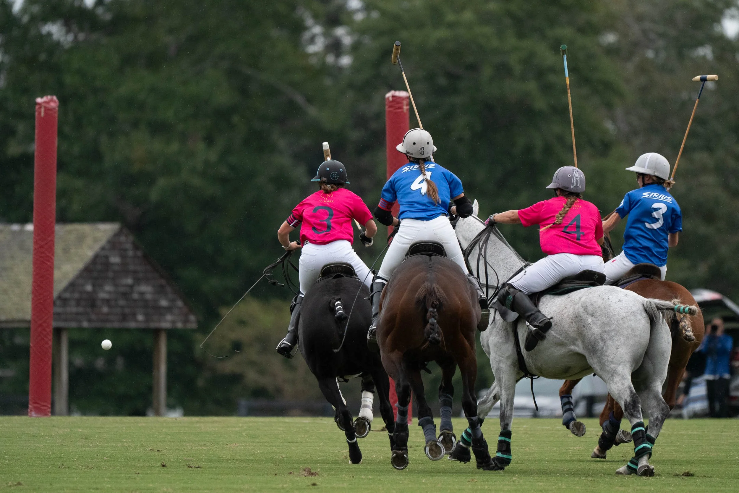 Polo players on horseback pursuing a ball during a match on a grassy field