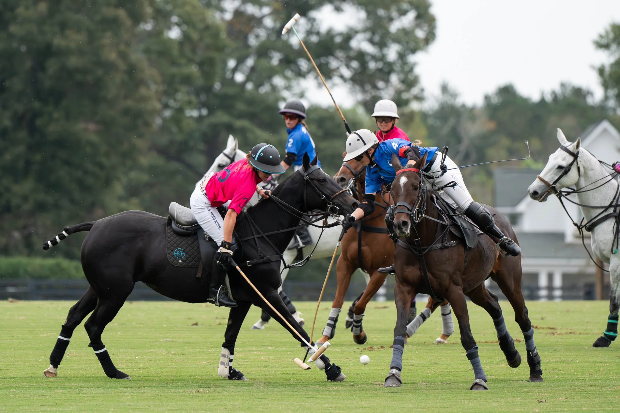 Polo players on horseback competing for the ball on a grassy field