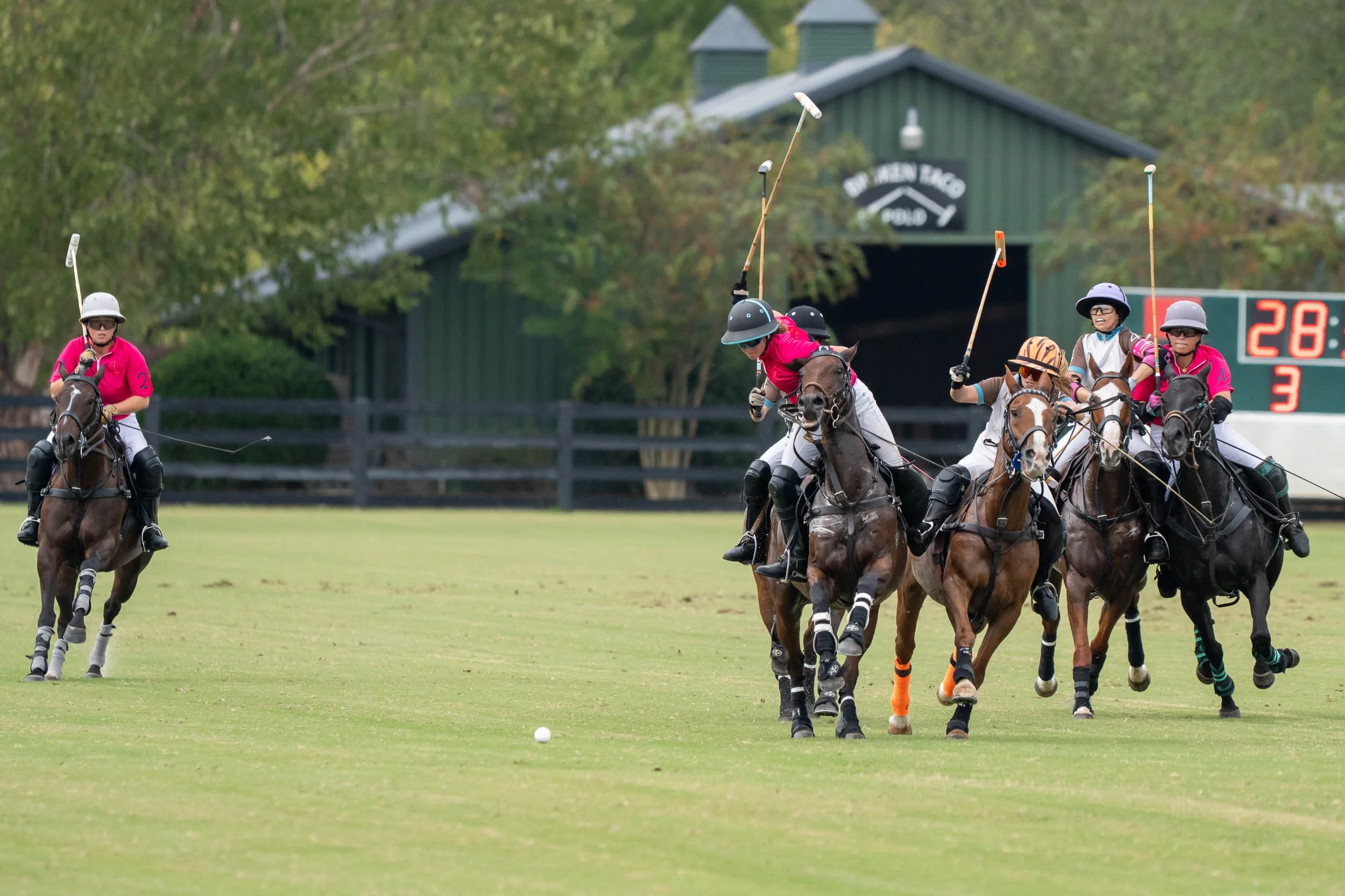 Polo players on horseback competing for the ball on a grass field.