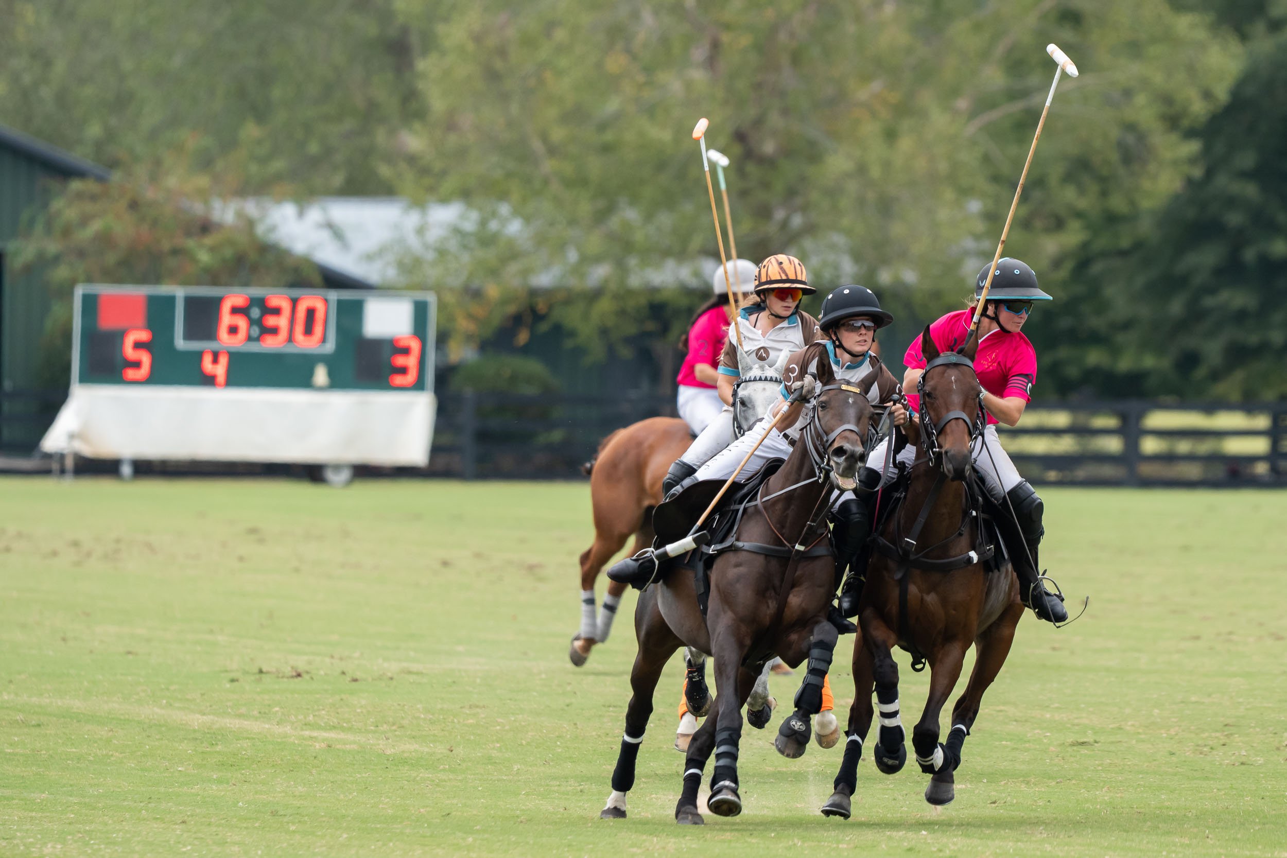 Polo players on horseback competing on a grass field while carrying mallets, with a digital scoreboard showing 6:30 and a 5–3 score.