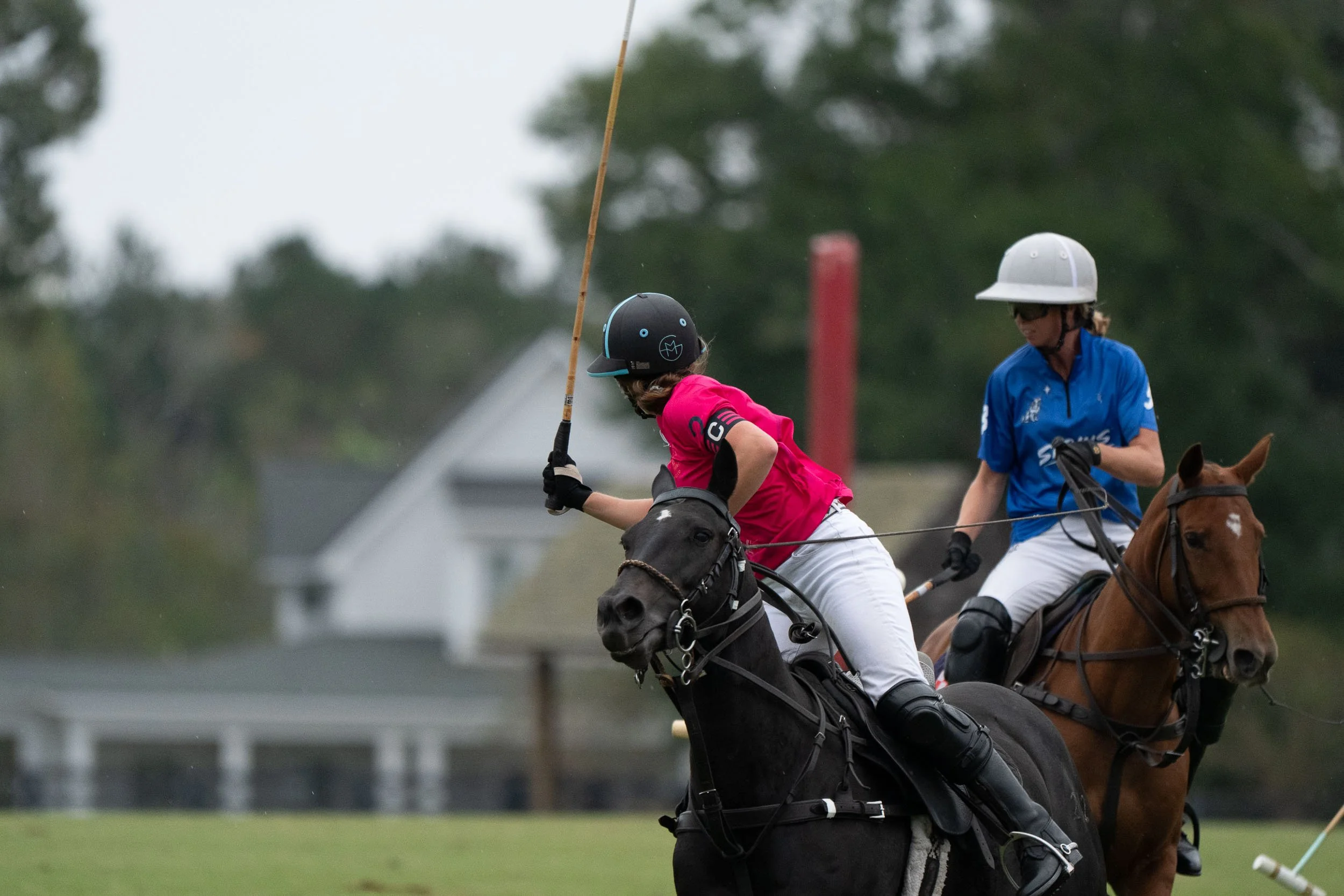 Polo players wearing helmets and riding horses during a match on a grassy field