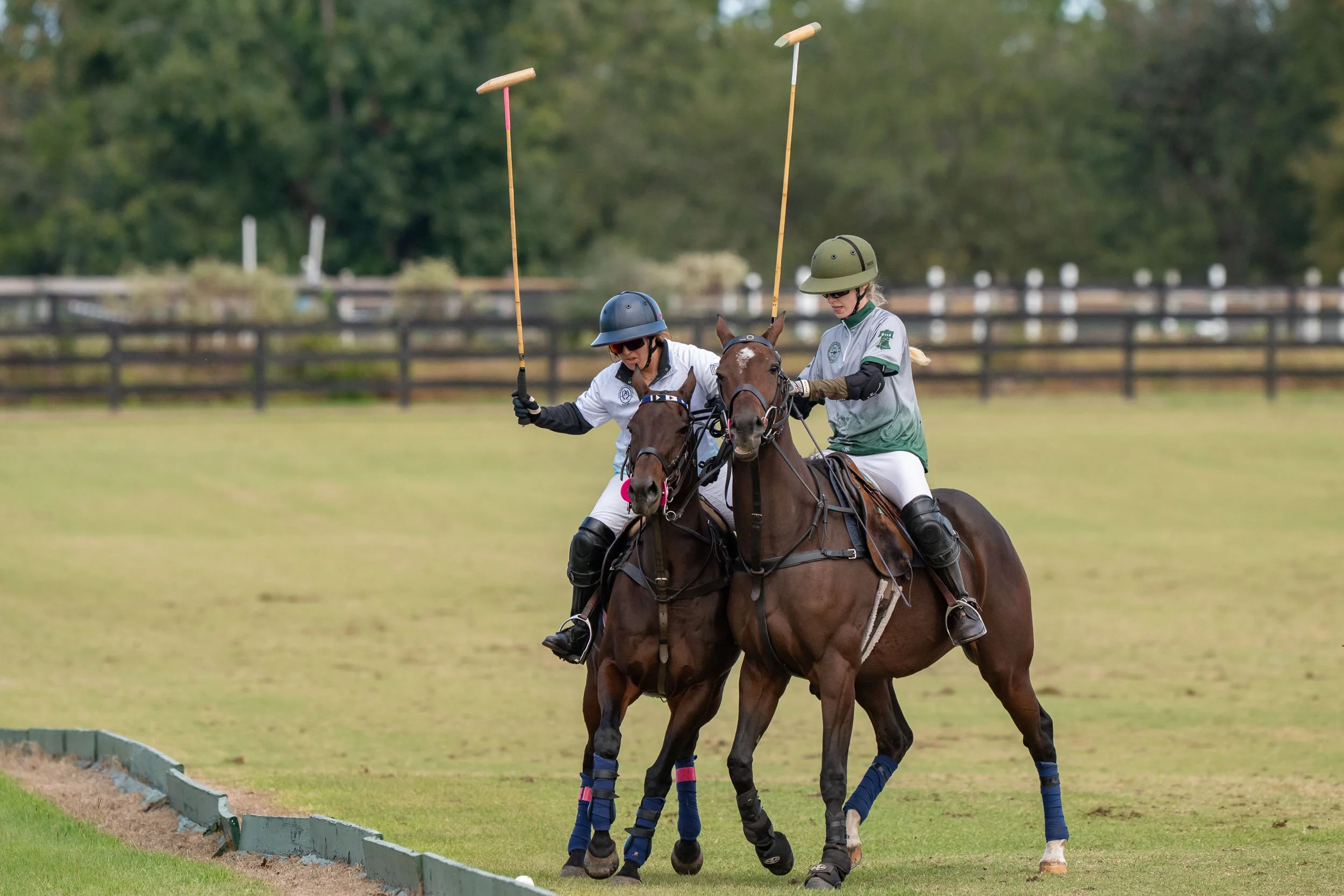 Two polo players riding horses on a grassy field, holding mallets during a polo match.