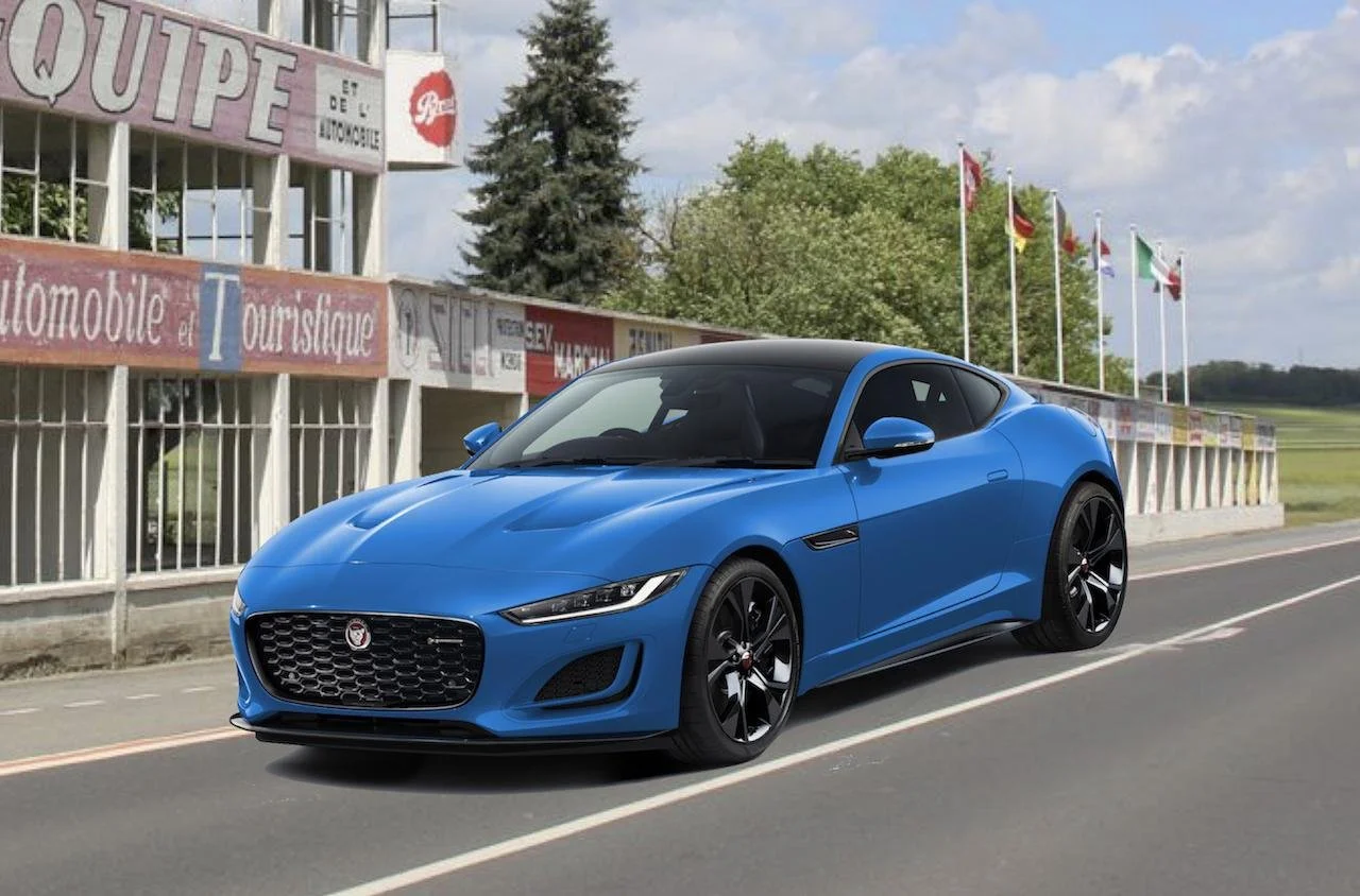 A blue sports car parked on the side of a road with a building and flags in the background.