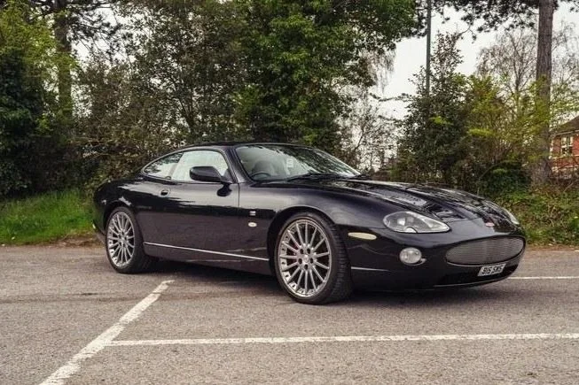 Black sports car parked in an empty parking lot with trees and bushes in the background.