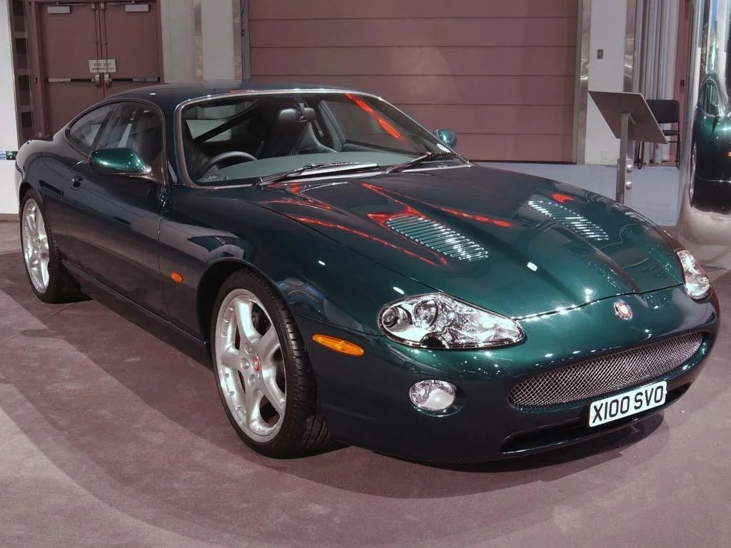 A dark green sports car on display indoors, with a license plate reading 'X100 SVO'