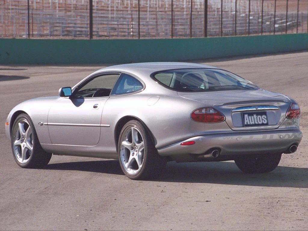 Silver sports car on a racetrack with a green wall and fencing in the background