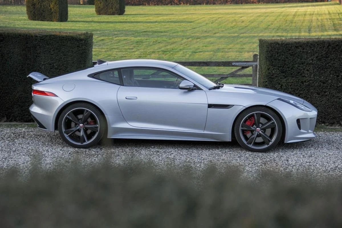 Silver sports car parked on gravel path beside neatly trimmed hedges and green lawn.