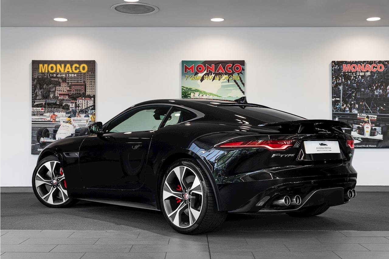 Black Jaguar F-Type sports car inside a showroom, with Monaco racing posters on the wall behind it.