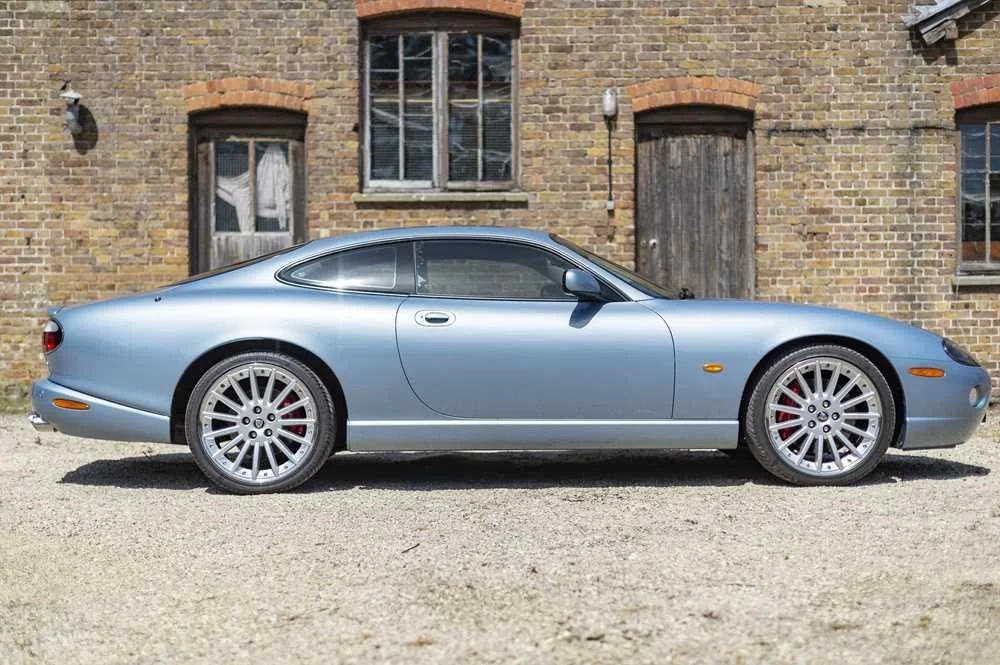 Silver sports car parked on a gravel driveway in front of an old brick building with boarded-up windows.