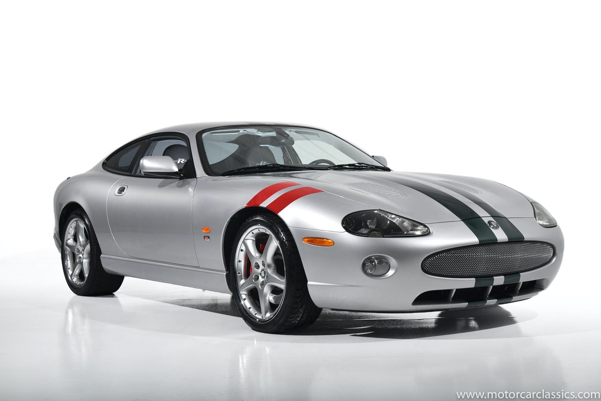 Silver sports car with black, red, and white racing stripes, parked on a plain white background.