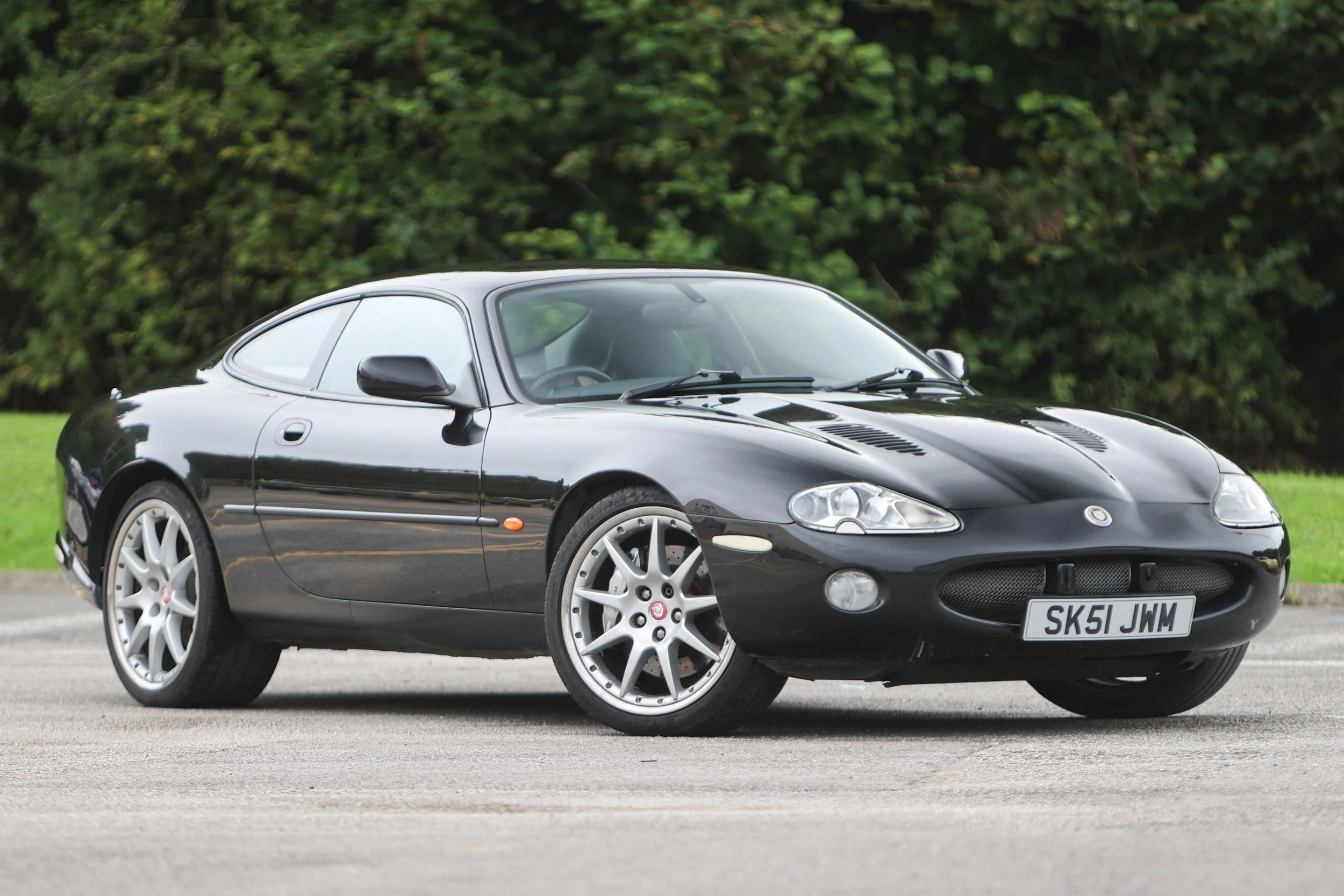 A black sports car parked on a paved surface with a background of green trees.