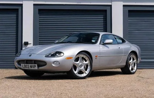 Silver sports car parked in front of a gray garage with closed doors.