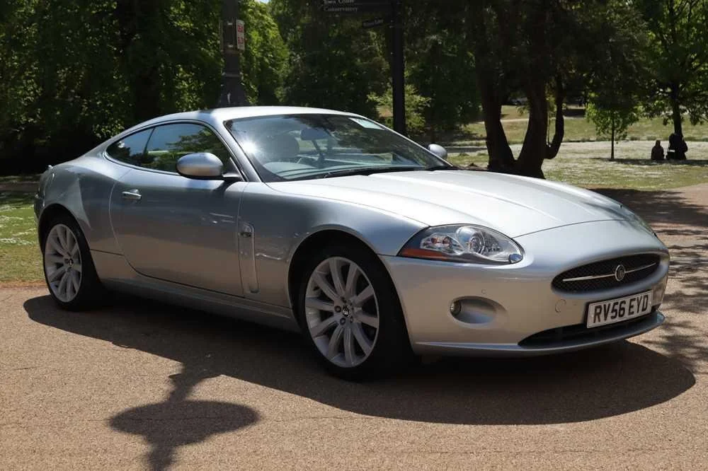 Silver sports coupe parked on a paved road with trees and grass in the background.