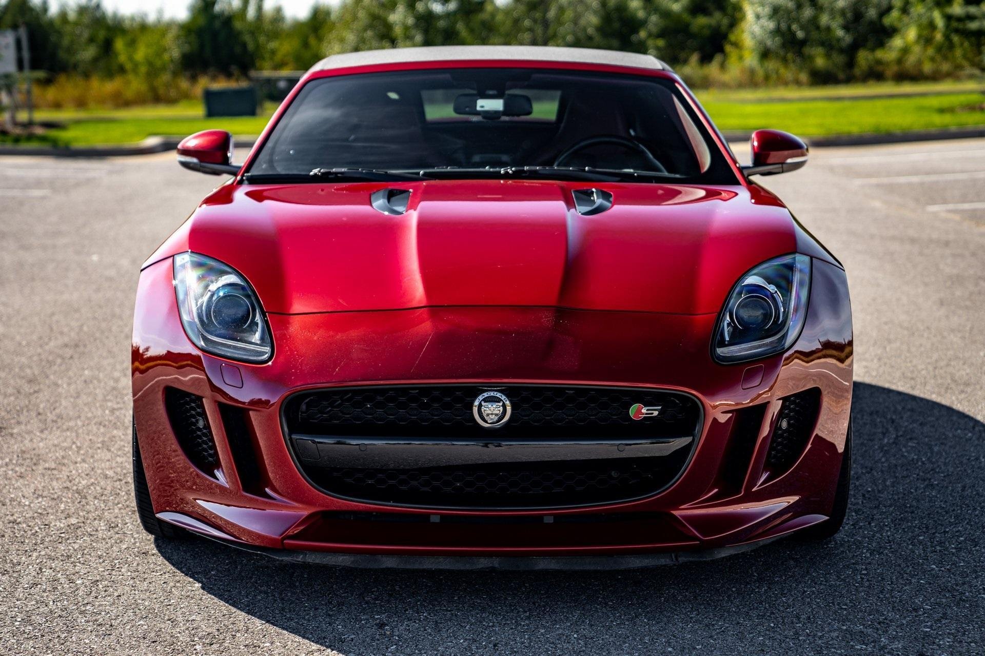 Front view of a red Jaguar F-Type sports car parked on a road with greenery in the background.